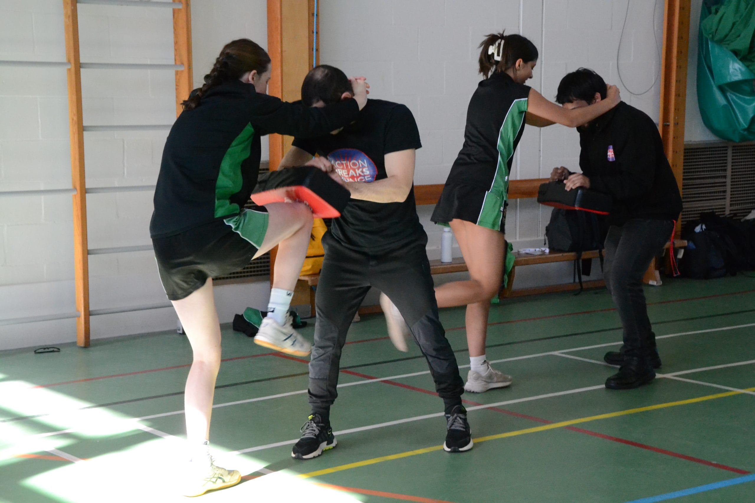 Two pupils taking part in a self-defence class, practicing using their knees to defend themselves